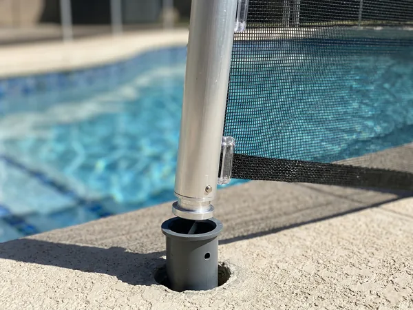 Close-up of removable pool fence showing transparent black mesh, aluminum post, and deck-mounted sleeve