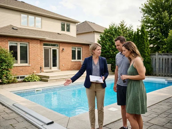 Couple and real estate agent standing at the edge of a backyard pool during a home showing