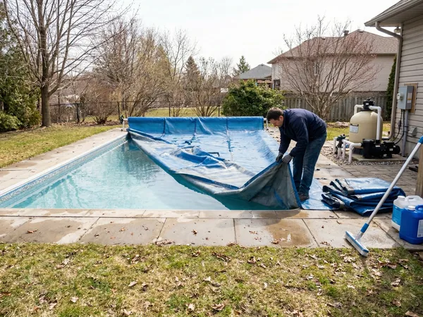 Residential inground pool mid-opening with winter cover being removed in early spring