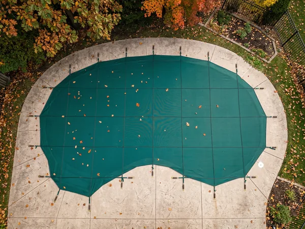 Overhead view of a mesh safety cover stretched taut over a residential pool with brass anchors in the deck